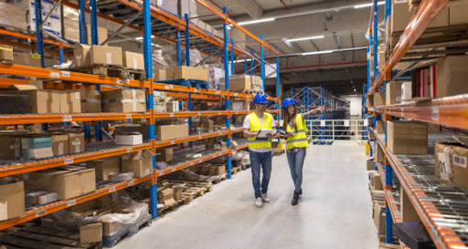 Two caucasian warehouse workers walking in distribution storage area discussing about logistics and organization.